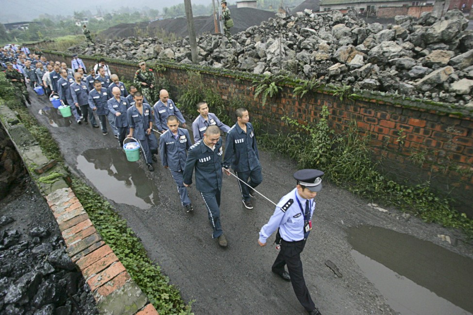 A policeman leads inmates as they walk along a road with their wrists tied together to a rope at Emei Mountain region