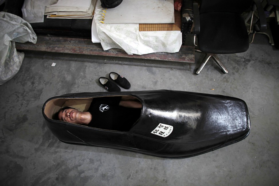 Chen Mingzhi, a shoe designer, lies inside of his handmade 1.9 metre-long right shoe at his family store in Wenling, Zhejiang province