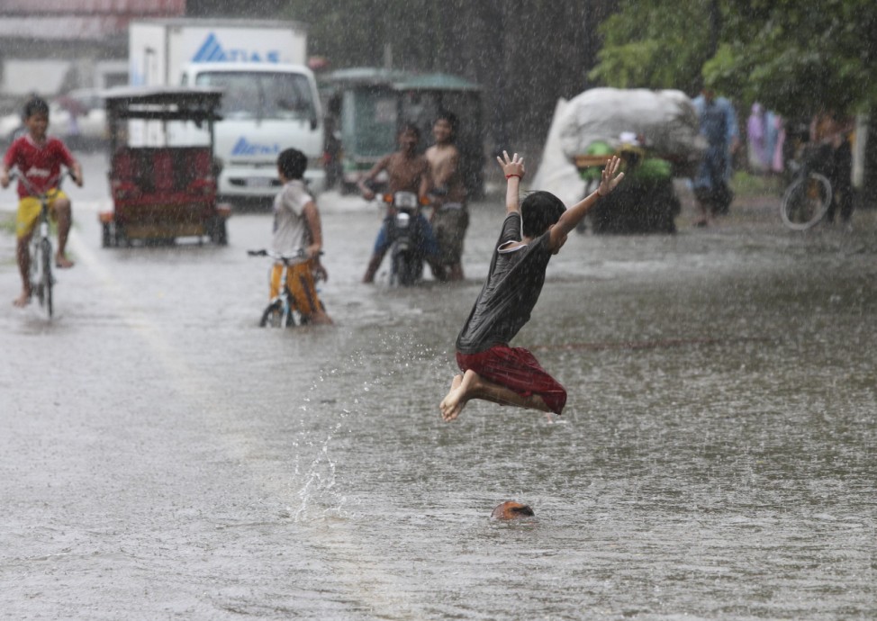 A boy plays on a flooded street near the Royal Palace during rainfall in central Phnom Penh