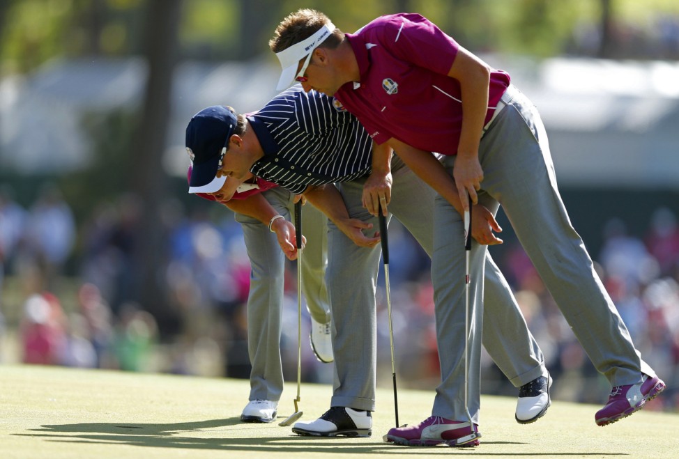 U.S. golfer Johnson looks at a divot on the third green with Team Europe golfers McIlroy and Poulter during the afternoon four-ball round at the 39th Ryder Cup golf matches at the Medinah Country Club