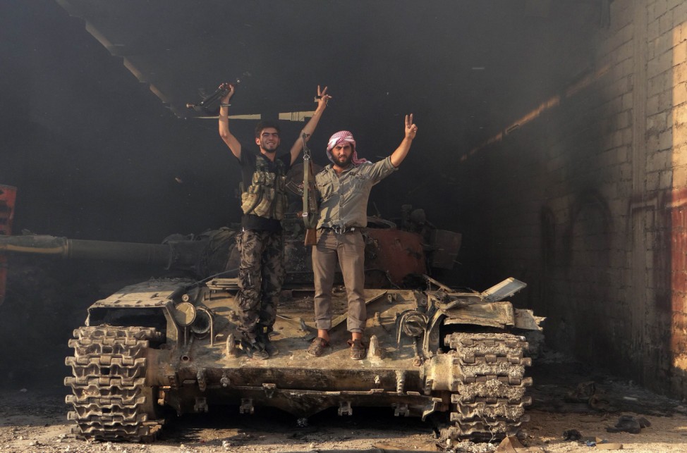 Two members of the Free Syrian Army stand on a tank as they gesture 'V' for victory in the Saraqib area near the northern city of Idlib