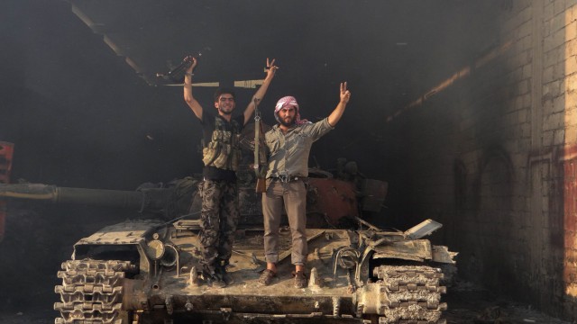 Two members of the Free Syrian Army stand on a tank as they gesture 'V' for victory in the Saraqib area near the northern city of Idlib
