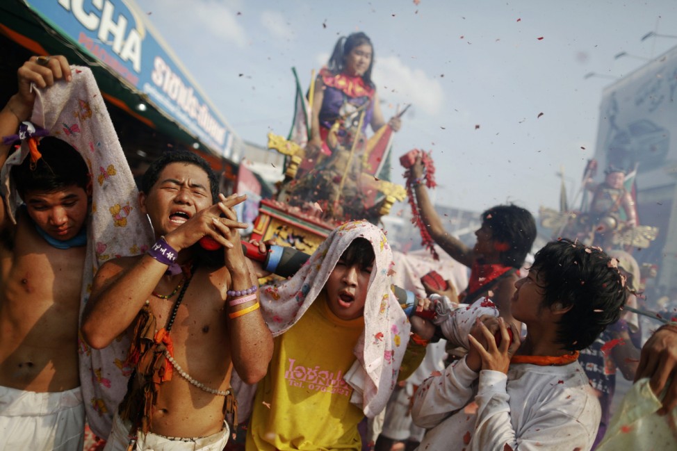 Devotees of the Chinese Bang Neow Shrine carry a statue and another devotee through exploding firecrackers during the annual vegetarian festival procession through central Phuket