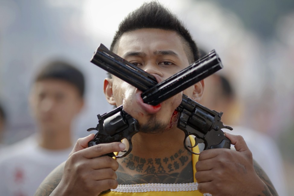 A devotee of the Chinese Bang Neow Shrine with two guns pierced through his cheeks takes a part in procession during the annual vegetarian festival in Phuket