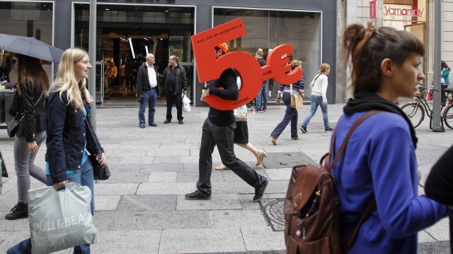 A man holds a foam cutout of five euros which is an advertisement for a shop as he walks in central Barcelona