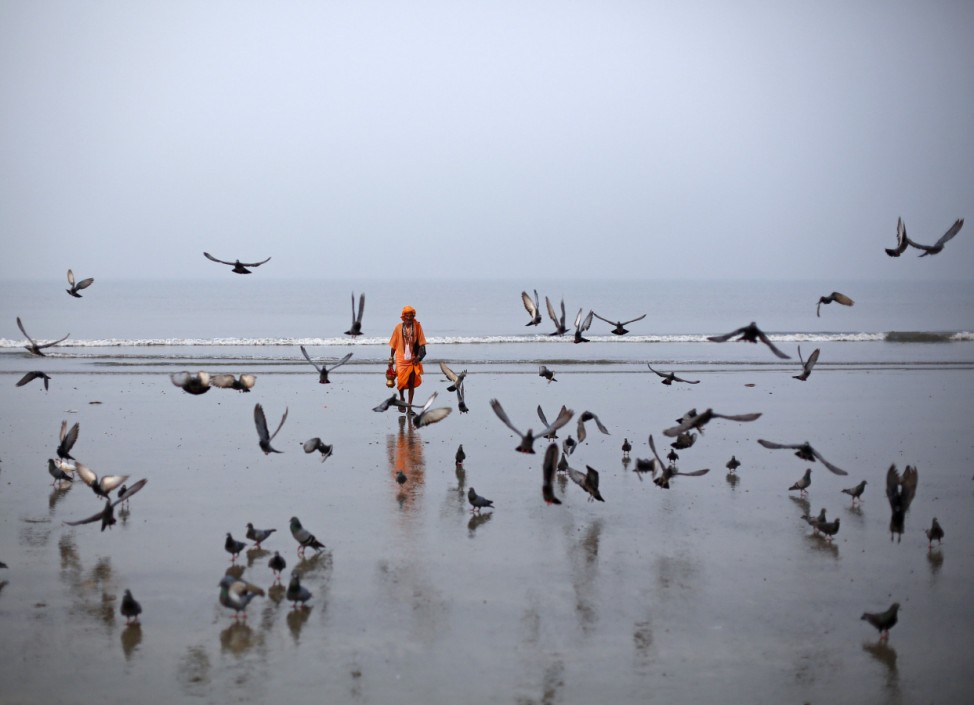 A Hindu holy man walks amongst birds flying at a beach along the Arabian Sea in Mumbai