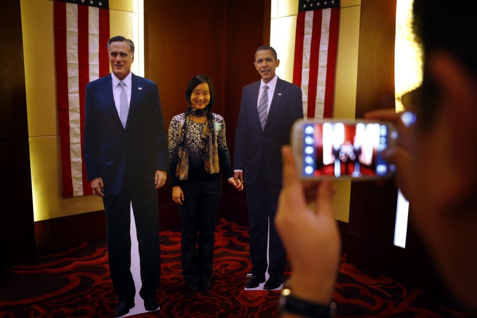 A guest at a Presidential election event, organised by the U.S. embassy, poses for her photograph with cardboard cut-outs of U.S. President Obama and Republican presidential nominee Romney in Beijing