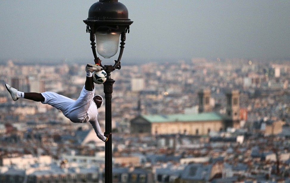 A soccer freestyler performs on a light pole next to the Montmartre Sacre Coeur Basilica in Paris