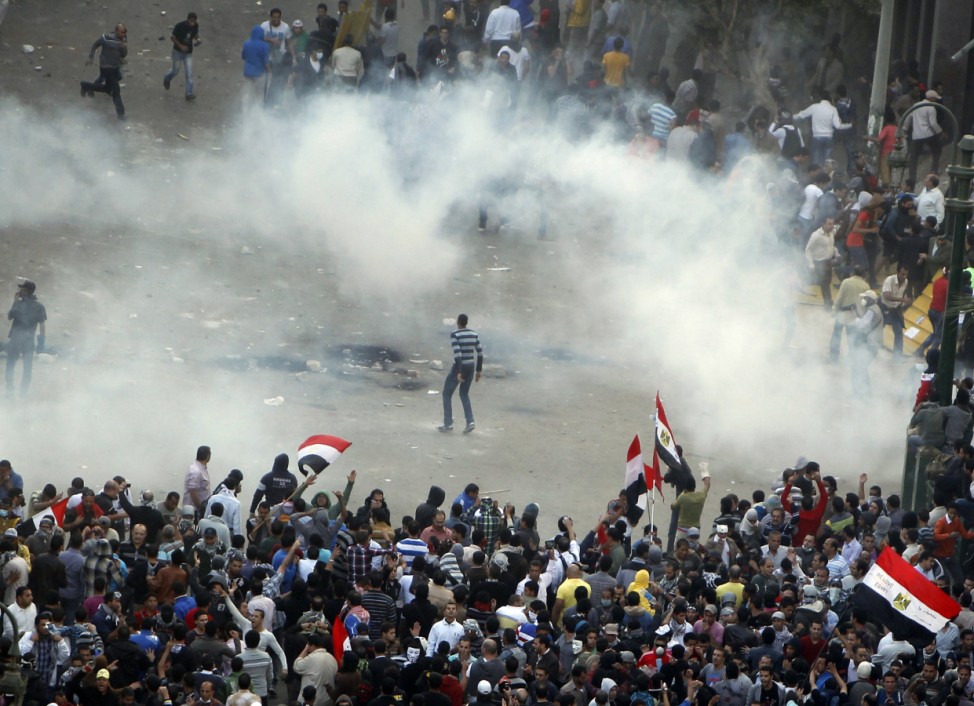 Protesters run from tear gas released by riot police during clashes at Tahrir square in Cairo