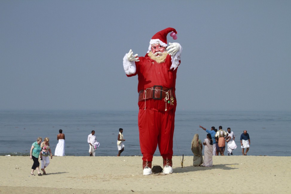 Tourists and locals walk past a Santa Claus statue placed on a beach for a film shoot in Kochi
