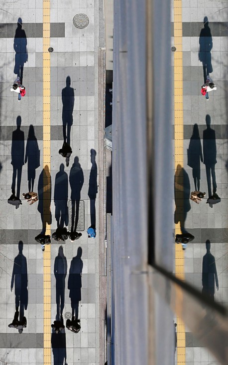 Pedestrians cast shadows on the sidewalk near the headquarters of the Bank of Japan in Tokyo