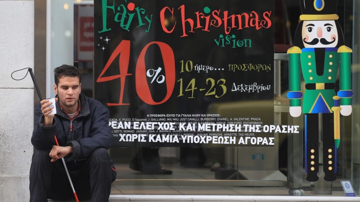 A blind beggar asks for alms outside a Christmas decorated shop i