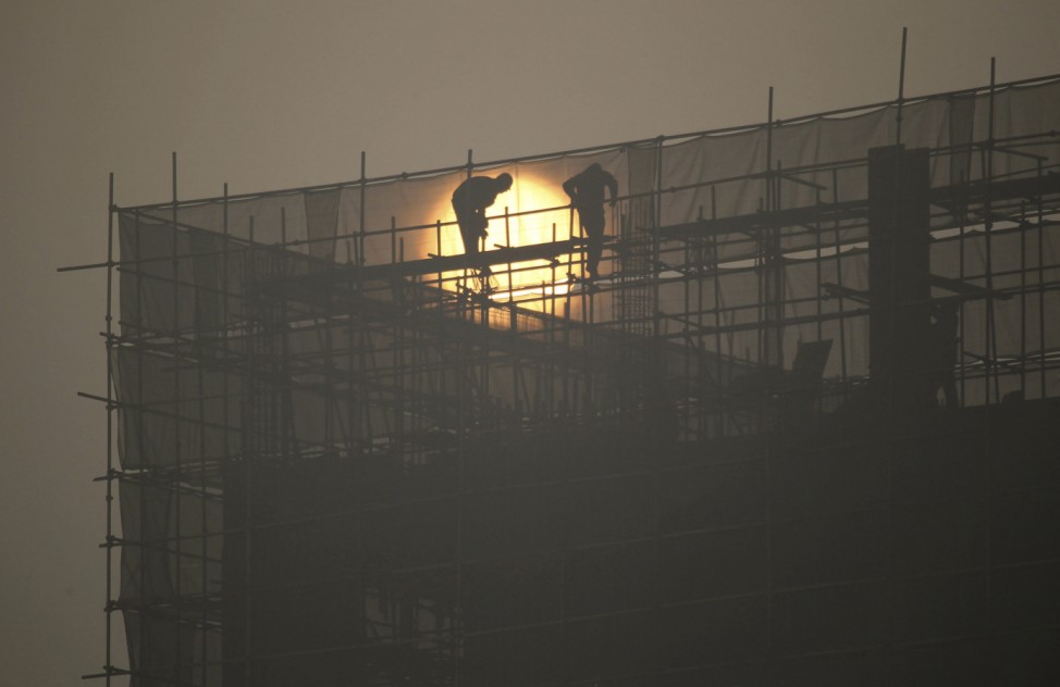 Labourers install scaffolding at a residential building construction site during sunrise on a hazy day in Zhengzhou