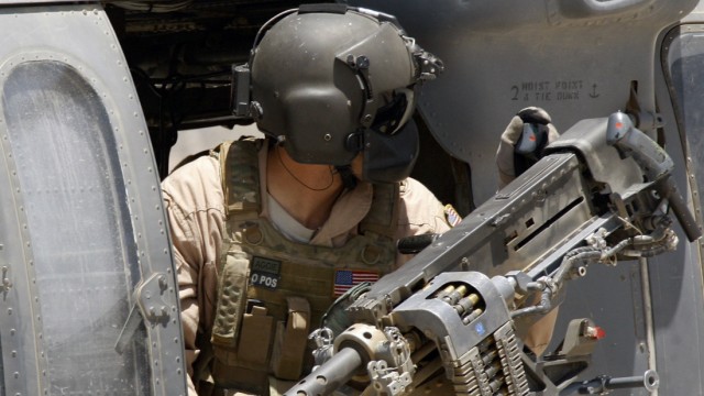U.S. Black Hawk helicopter gunman checks his heavy machine gun while leaving Camp Nathan Smith in Kandahar City