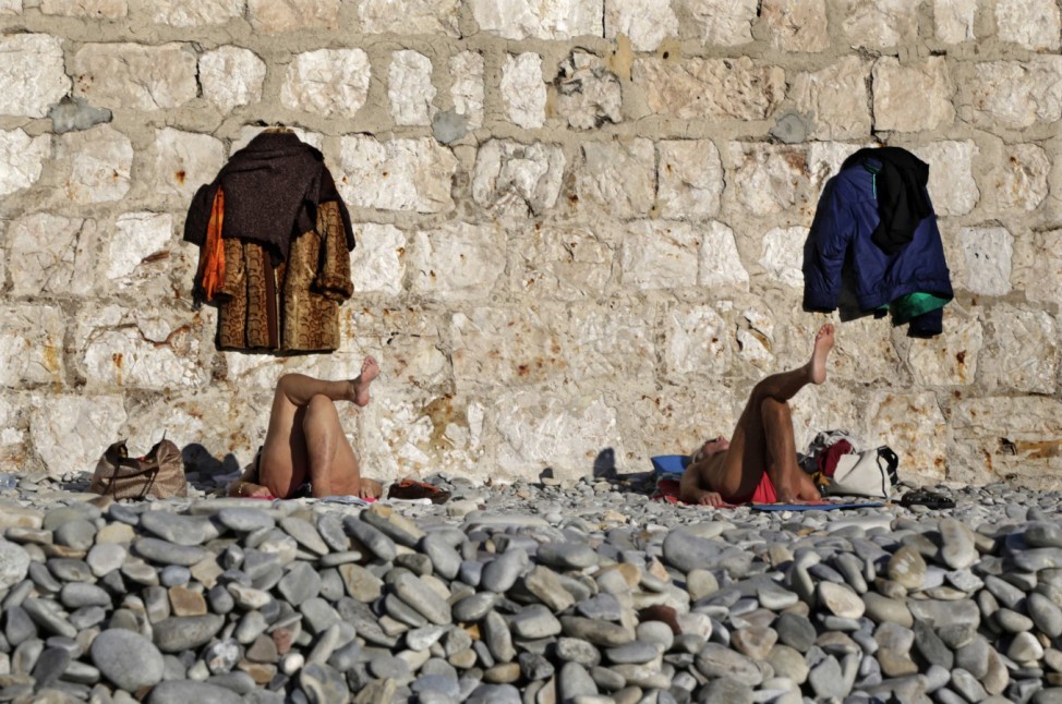 Coats are hung on a wall as people sunbathe on the beach in Nice