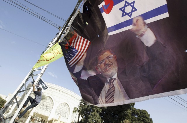 A protester climbs a pole near a banner depicting President Mursi holding Israeli and American flags, in front of presidential palace in Cairo