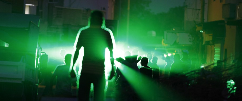 Anti-government protesters shout slogans while standing in front of laser beams emitted by riot police in the village of Diraz west of Manama