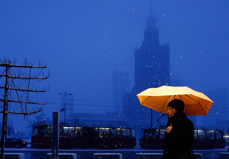 A woman holds an umbrella as she walks in front of the Palace of Culture during a winter day in central Warsaw