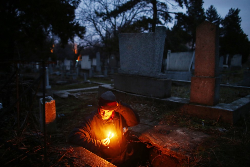 Bratislav Stojanovic, a homeless man, holds candles as walks out of a tomb where he lives in southern Serbian town of Nis