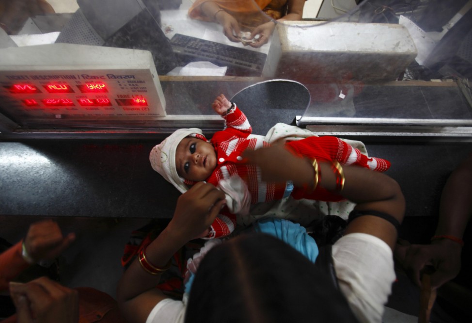 A woman rests her child on the ticket counter as she buys a train ticket at Allahabad Railway Station