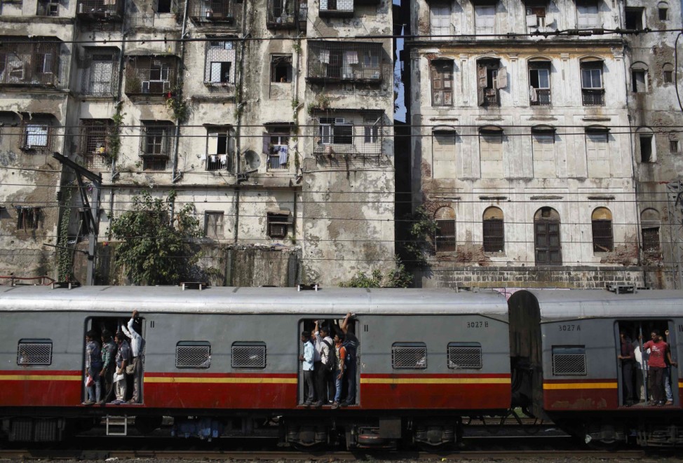 Commuters stand at the open doorways of a suburban train as they head toward their destination in Mumbai