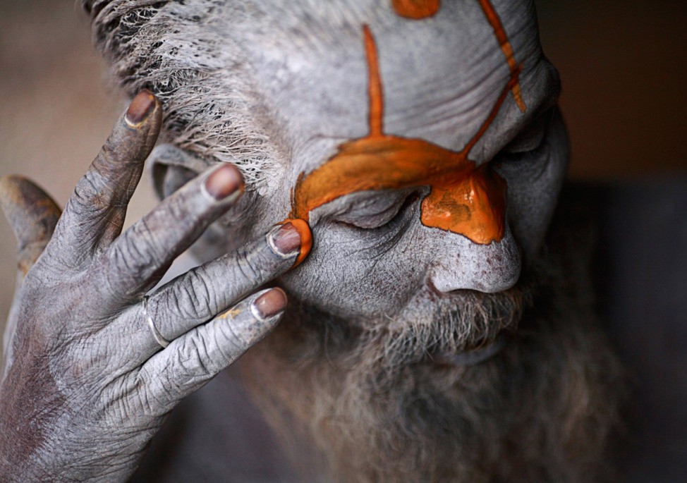 Hindu sadhu applies paint to his forehead at his ashram on the premises of Pashupatinath Temple in Kathmandu