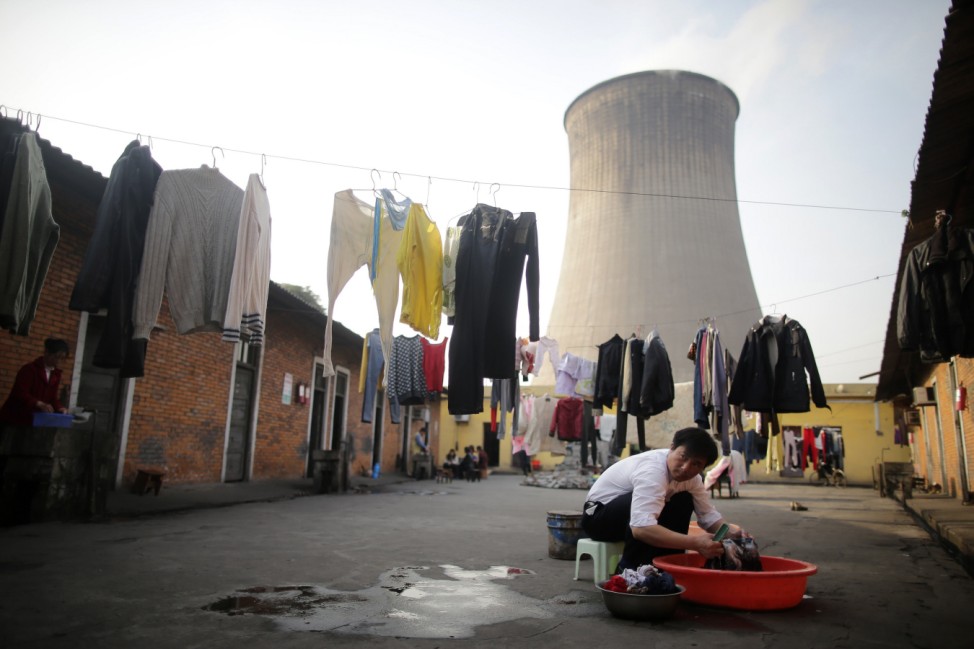A resident washes clothes in a yard in front of a water-cooling tower of Wuhan Iron And Steel Corp, in Wuhan