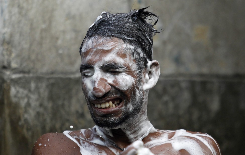 A man reacts as soap enters his eyes at a public well early morning before starting work in Colombo