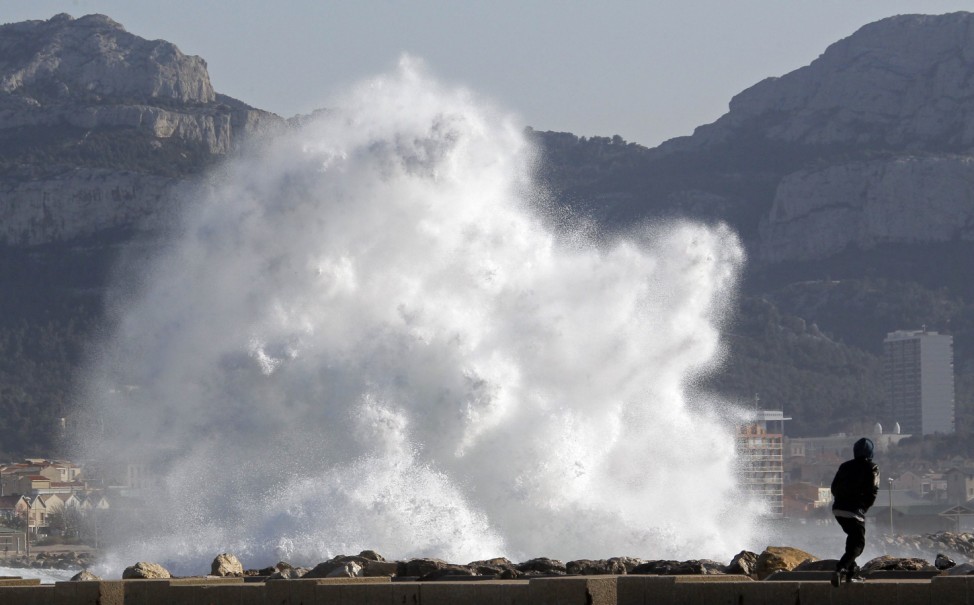 A passer-by walks as a high wave hits the waterfront in Marseille