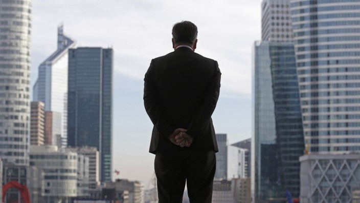 A businessman looks on as he stands under the Arche de la Defense in the financial district west of Paris