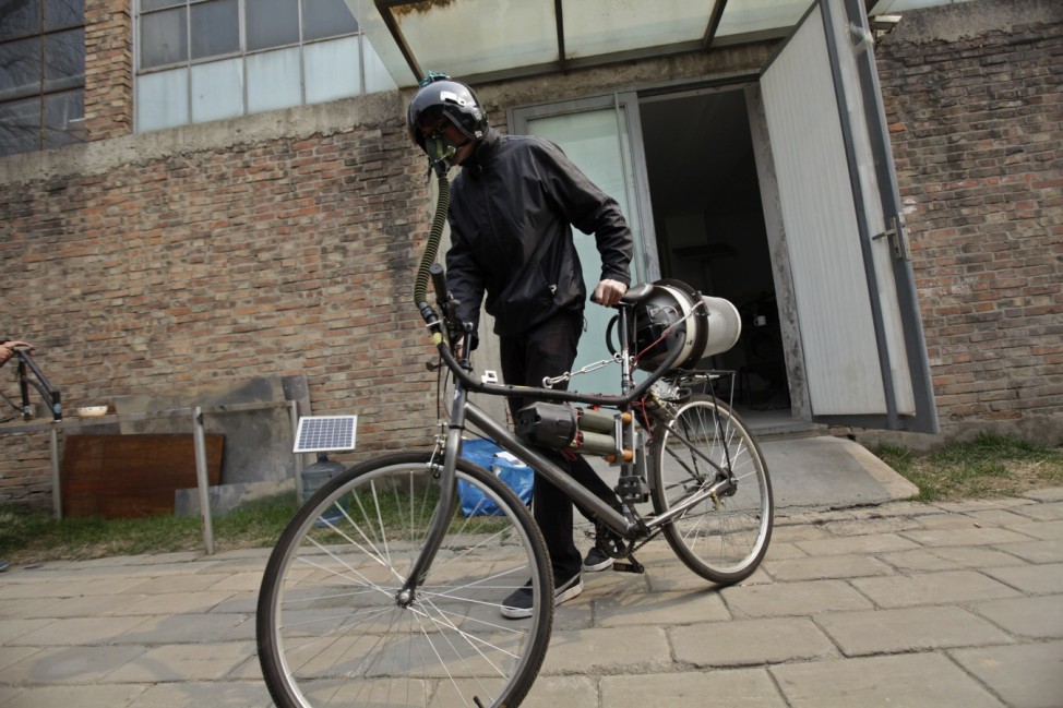 Artist Matt Hope, wearing a helmet, pushes his air filtration bike out from his studio on a hazy day in Beijing