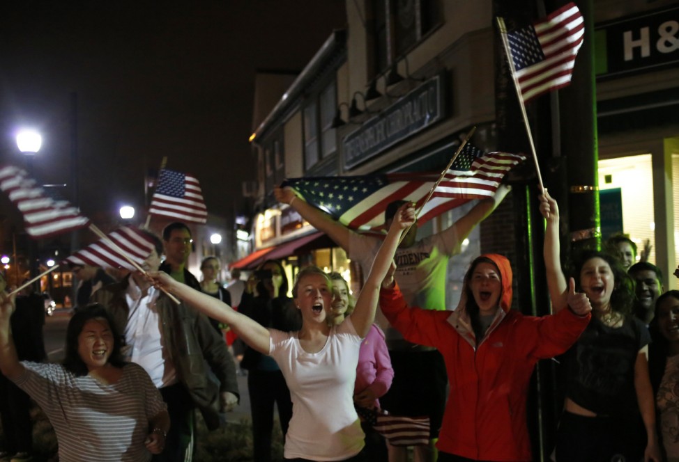 People wave U.S. flags while cheering as police drive down Arlington street in Watertown