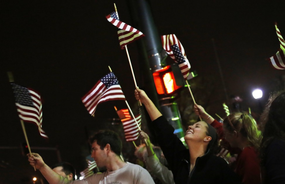 People wave U.S. flags while cheering as police drive down Arlington street in Watertown