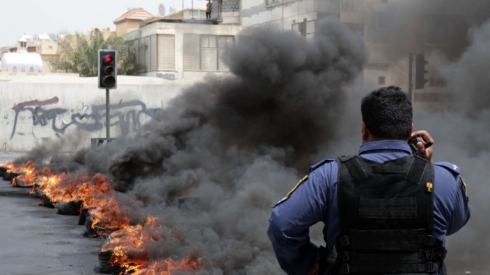 Riot police officer stands in front of a line of burning tyres in the early hours of morning in Manama