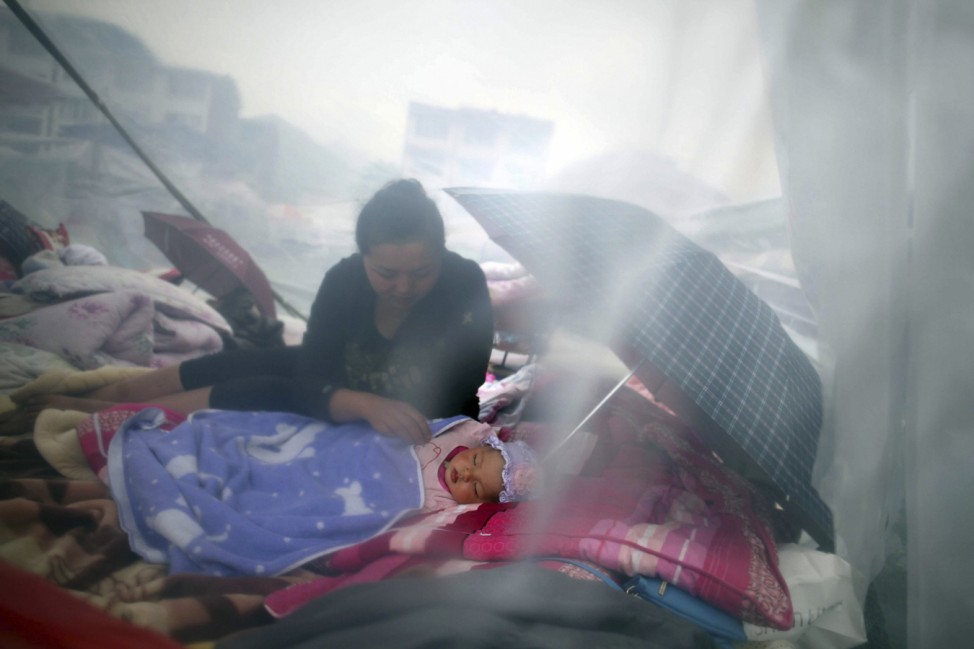 A woman looks at her child as they rest among the wreckage after Saturday's earthquake in Lingguan town of Baoxing county