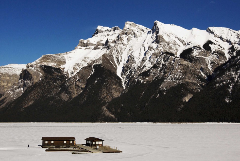 A man walks over a frozen Lake Minnewanka to a boathouse in front of the Canadian Rocky Mountains in Banff, Alberta