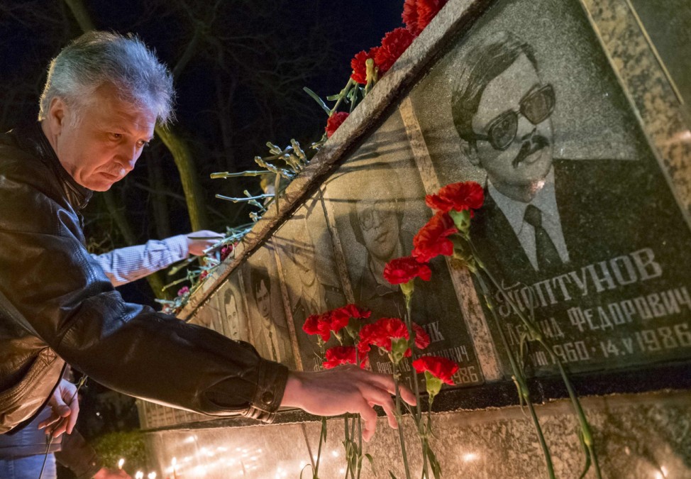 A man lays flowers at a memorial, dedicated to firefighters and workers who died after the Chernobyl nuclear disaster, during a night service in Slavutych