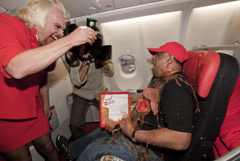 British entrepreneur Richard Branson, wearing an AirAsia flight attendant's uniform, drops a tray of drinks onto AirAsia's Chief Executive Tony Fernandes during an AirAsia promotional event on a flight from Perth to Kuala Lumpur