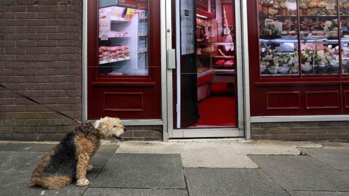 A man walks his dog past a vacant shop, with graphics pasted to the outside to make it look like working butchers shop, in the village of Belcoo, Northern Ireland