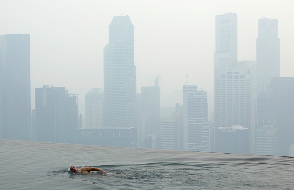 A hotel guest swims in the pool of the Marina Bay Sands Skypark overlooking the haze covered skyline of Singapore
