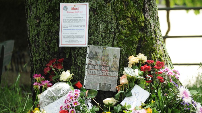Ermittlungen zum Isarmord: Blumen und Botschaften liegen beim Tatort, an dem der Radfahrer erstochen worden ist. Am Baumstamm hängen ein Zeitungsartikel und das Fahndungsplakat.
