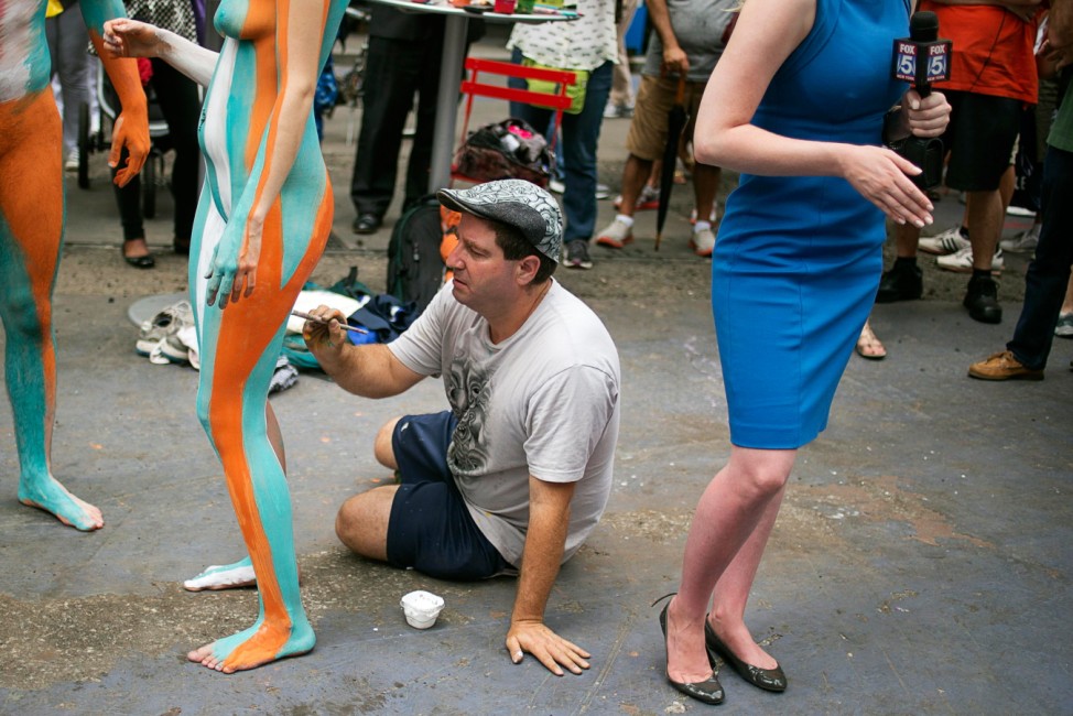 Artist Andy Golub places body paint on model Gianna James as a television journalist reports in Times Square, New York