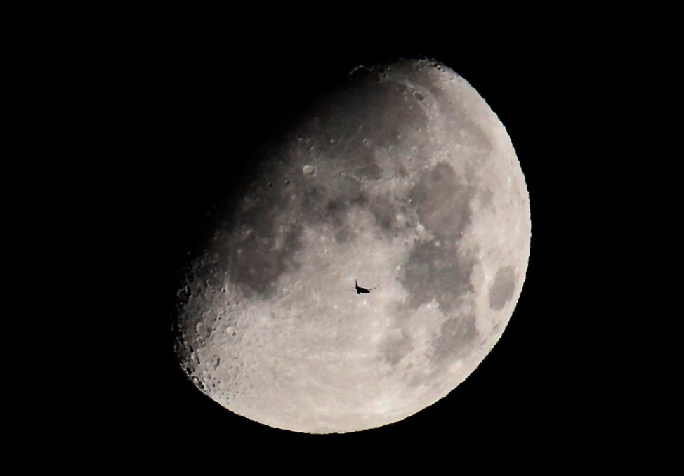 A passenger jet is silhouetted against the moon as it flies over Shanghai