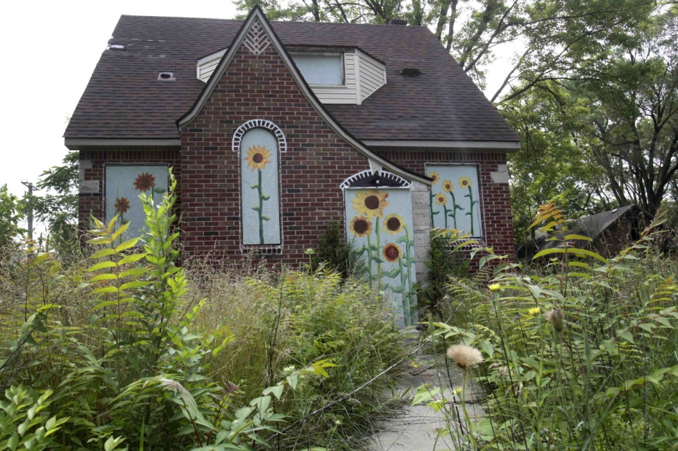 Overgrown grass and weeds are seen around a vacant house that has flowers painted on the boards to keep vandals out in the  Brightmoor neighborhood of Detroit