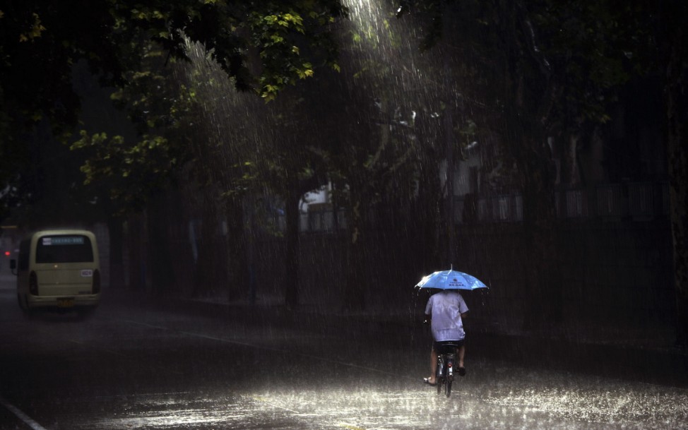 A man holds an umbrella as he rides along a street during a heavy rain in Jinan