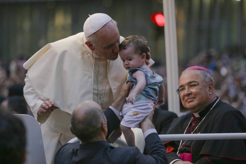Pope Francis kisses a baby while greeting a crowd of the faithful from his Popemobile in downtown Rio de Janeiro