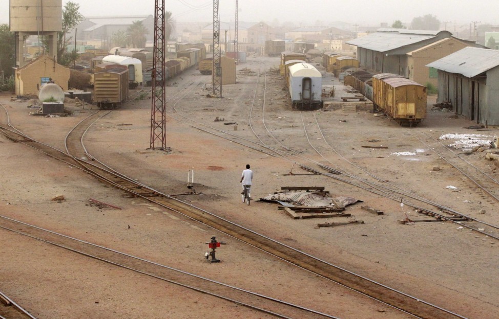 A man rides a bicycle past old trains at the Atbra Railway Station at the River Nile State
