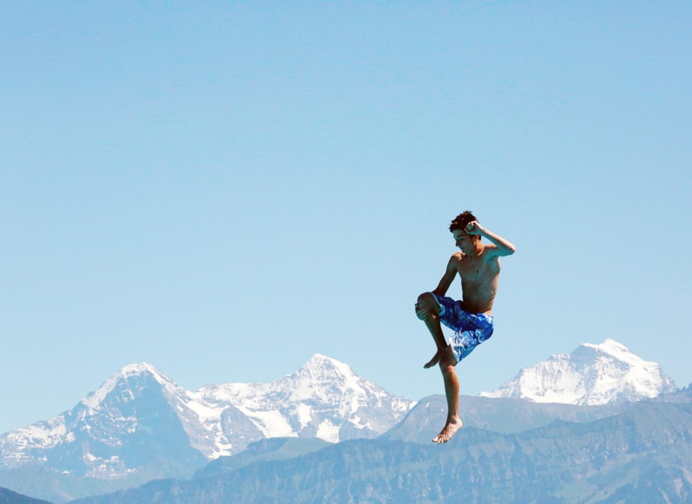 A boy jumps from a diving platform in front of the mountains Eiger Moench and Jungfrau in a public swimming pool in Thun