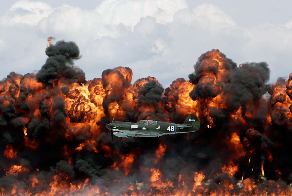 A World War II American plane flies in front of a wall of fire as it takes part in a re-enactment of the attack on Pearl Harbor during an afternoon air show at the EAA AirVenture at Wittman Regional Airport in Oshkosh