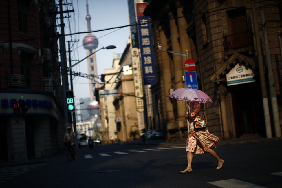 Woman uses an umbrella to protect herself from the sun as she crosses a busy street in downtown Shanghai